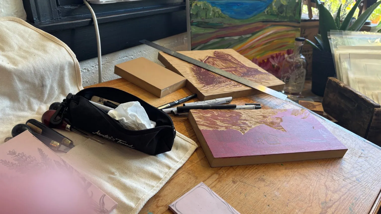 Two wooden print blocks with drawn scenes beside a set of marker pens on a table.